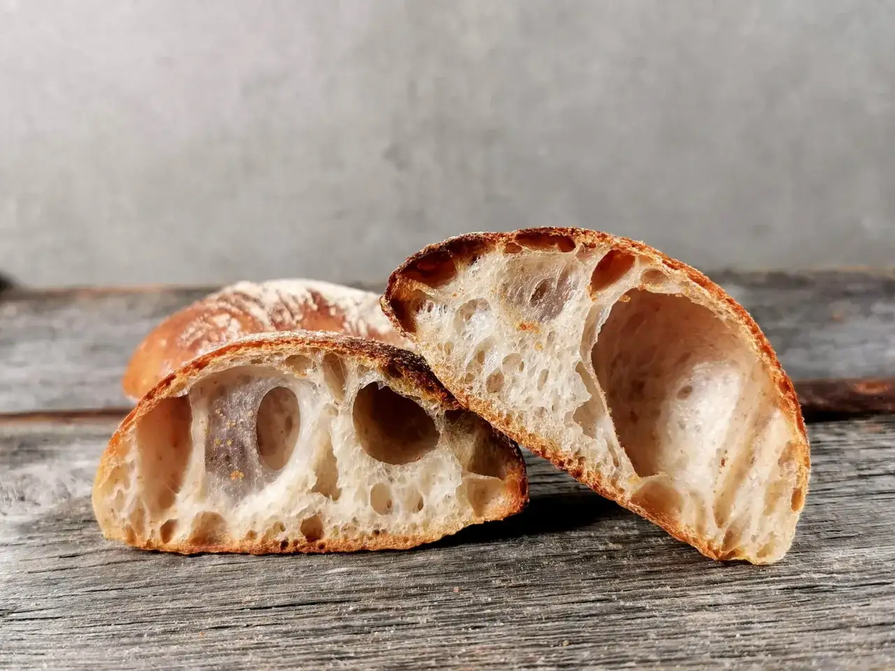 Zwei H&auml;lften eines rustikalen ciabatta mit sauerteig Brotes liegen auf Holzbrettern. Die Krume ist luftig und voller gro&szlig;er Blasen.