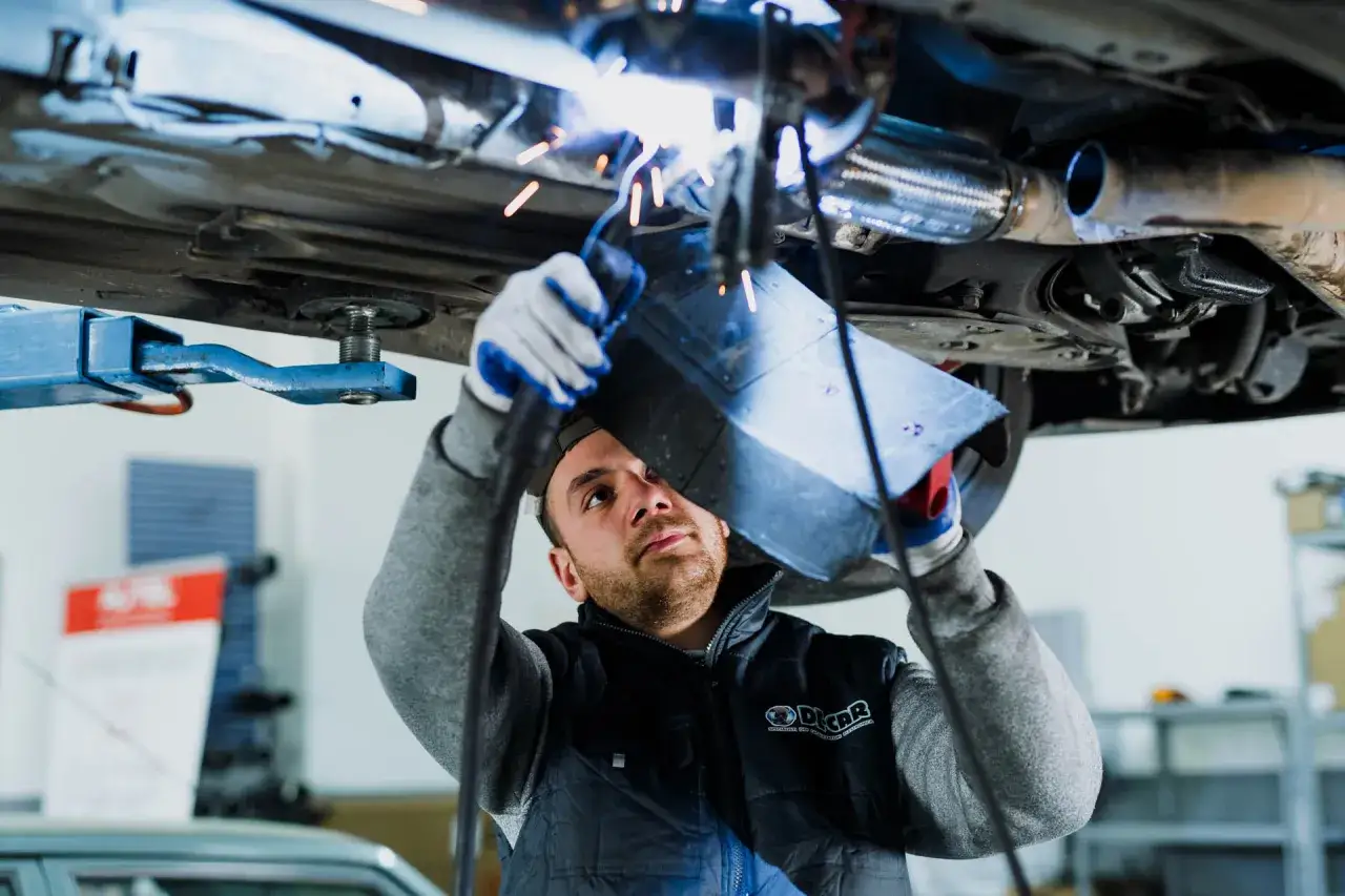 Meccanico esegue saldatura per rigenerazione forzata FAP su un'auto sollevata.