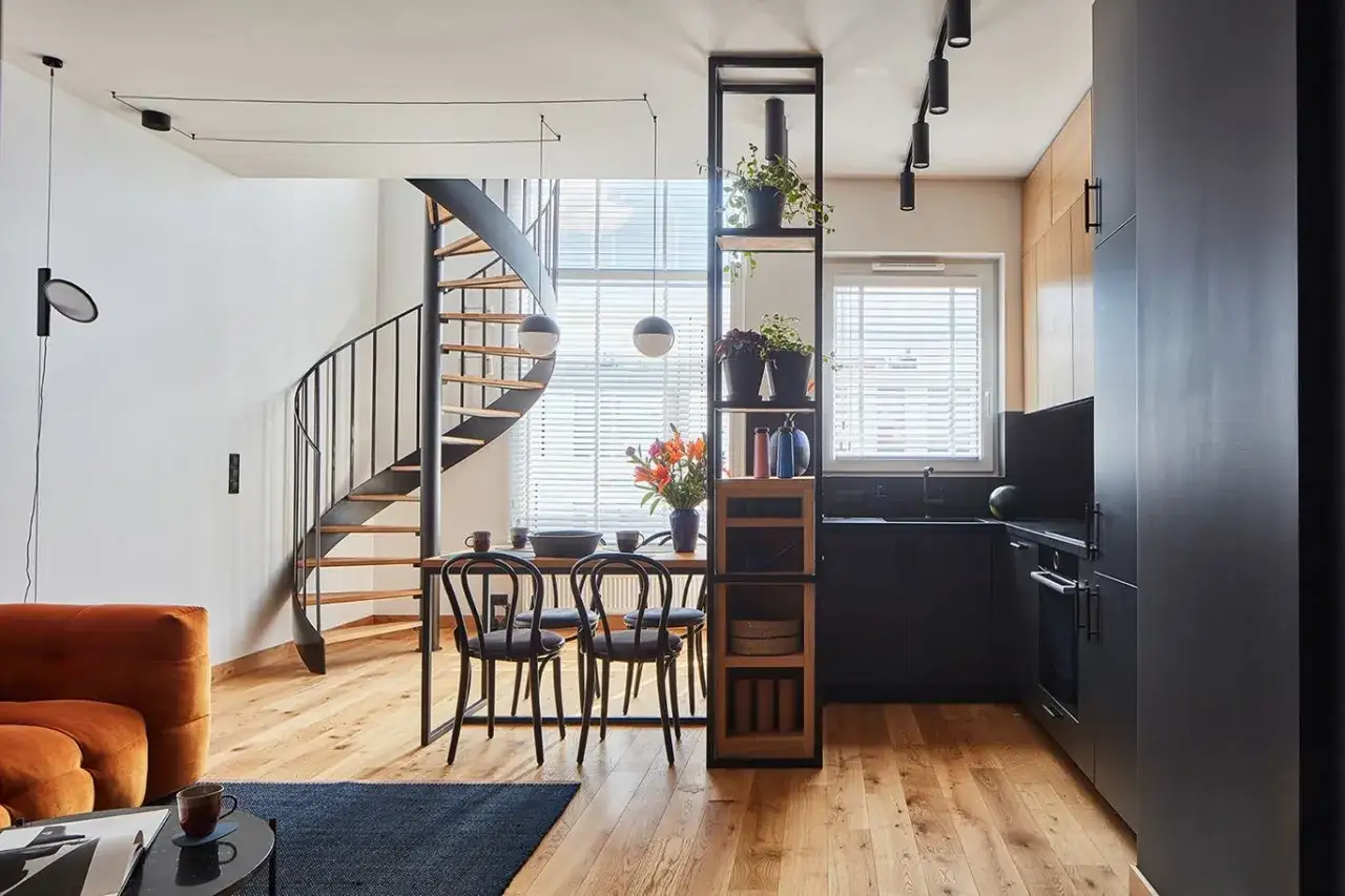 Nowoczesny salon w stylu loft z krętymi schodami, czarną kuchnią i pomarańczową kanapą. Aranżacje zachwycają.