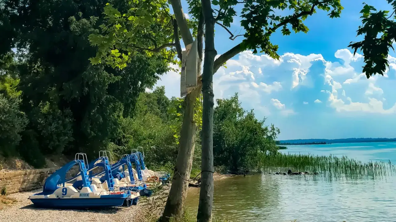 Rowerki wodne czekają na gości na plaży w Piani di Clodia. Piękny dzień nad jeziorem.