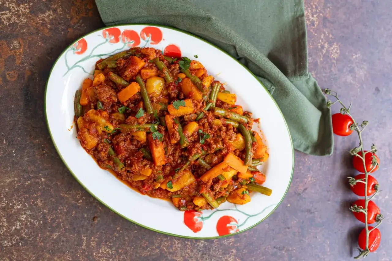 Plat de viande hachée et légumes, une recette simple et savoureuse. Haricots verts, carottes et pommes de terre se mêlent à la viande dans une sauce tomate.