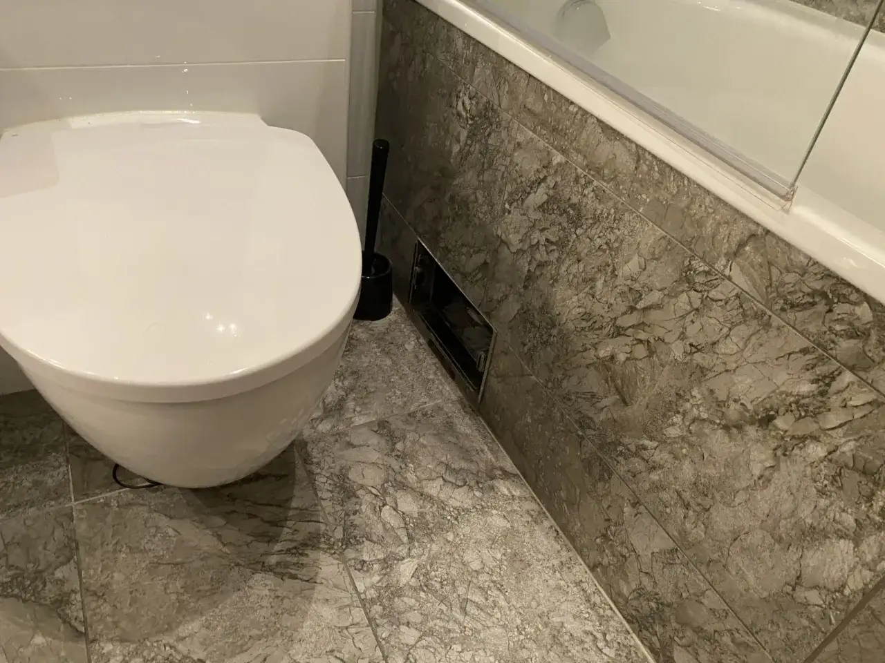 En toalett och badkar i ett modernt badrum. En toalettborste står bredvid toaletten. Kanske en dålig lukt avlopp kan förklara varför borsten behövs.