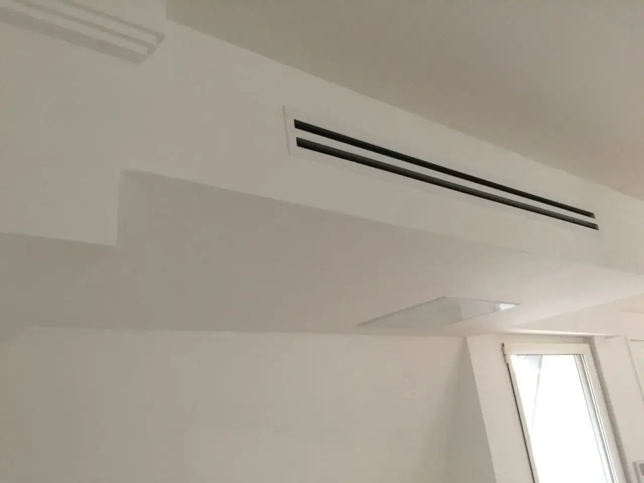 Ventilation discrète intégrée au plafond blanc, assurant un confort thermique invisible.