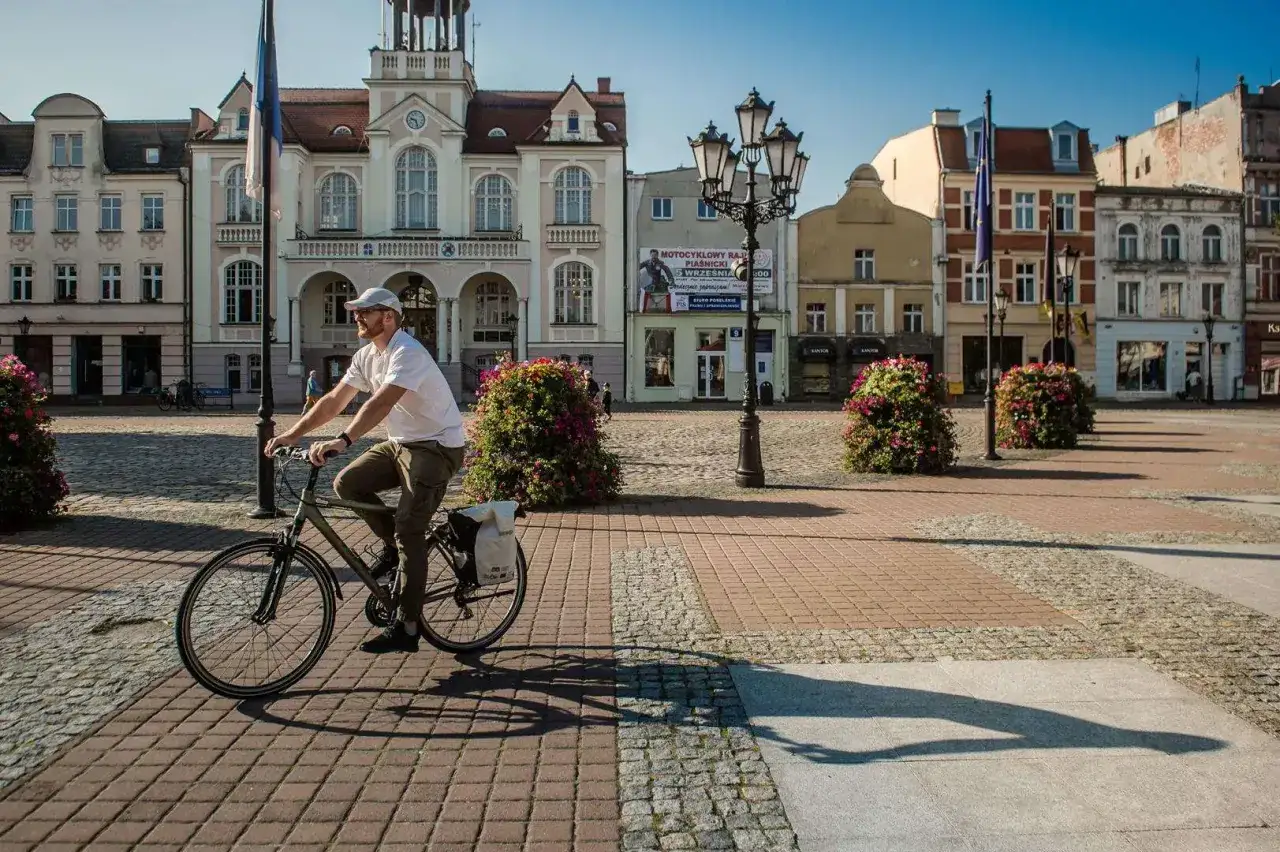 Mężczyzna na rowerze przemierza urokliwą **trasę w Wejherowie**, mijając zabytkowe kamienice i kwitnące krzewy.