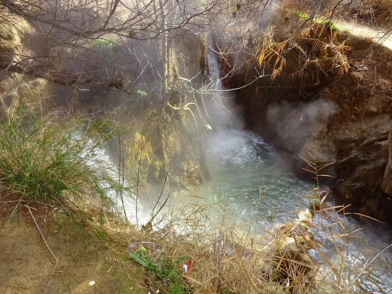 Vapor ascendente de las **aguas termales Santa Fe**, un remanso natural con vegetaci&oacute;n y rocas.