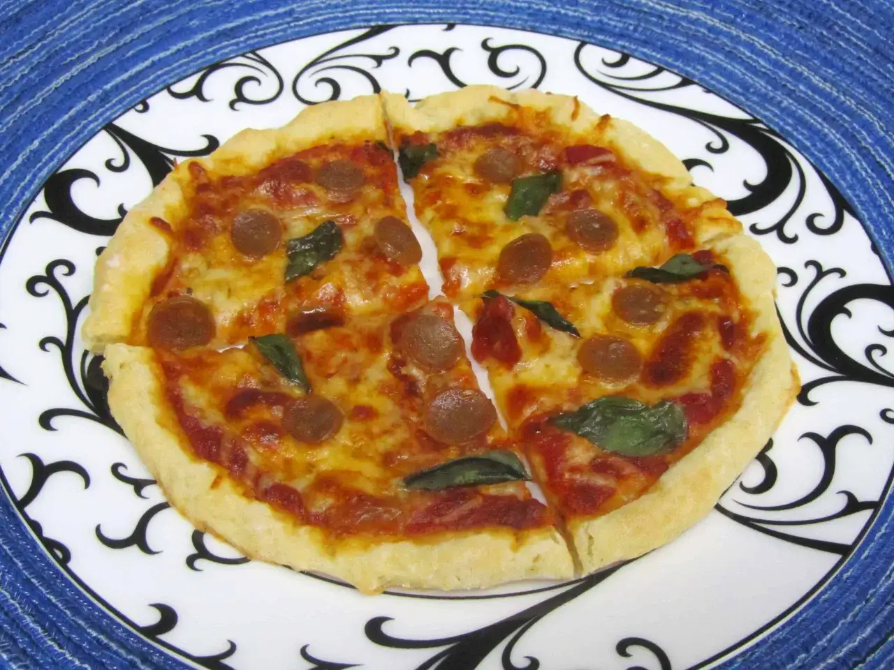 Idealna pizza dla jednej osoby, z ciągnącym serem, kawałkami kiełbaski i listkami bazylii, podana na ozdobnym talerzu.