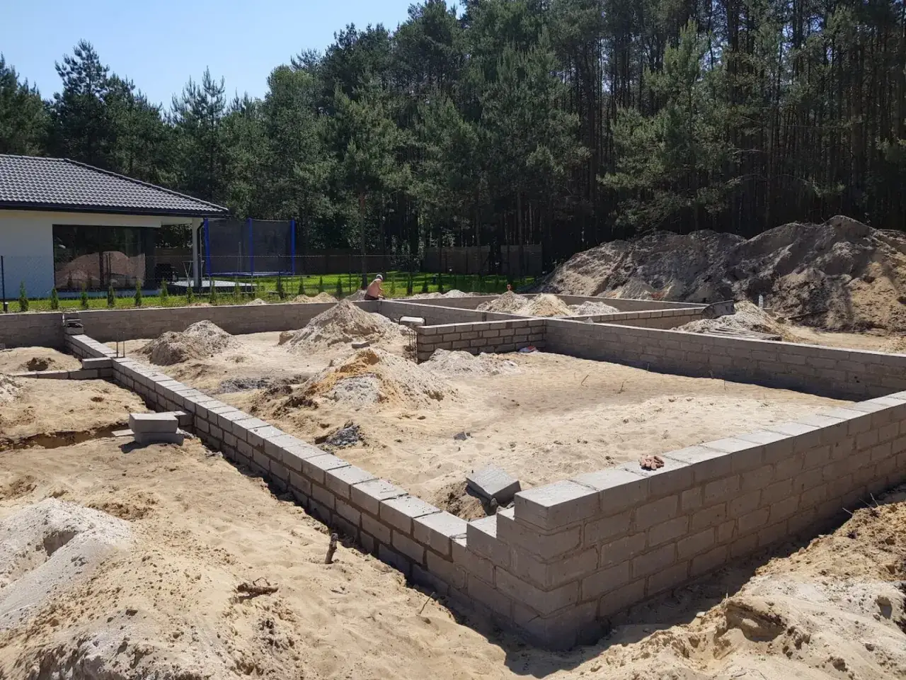 Fundamenty domu w budowie. Piasek, bloczki betonowe, koparka. Określenie ceny robocizny budowy domu za m2 wymaga analizy postępu prac.