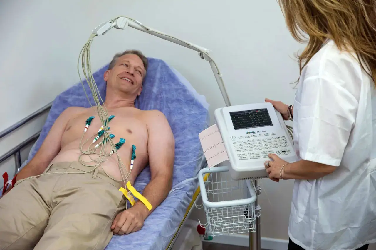Mężczyzna leży podłączony do aparatu EKG. Badanie ekg spoczynkowe ile trwa? Zwykle kilka minut, aby uzyskać dokładny obraz pracy serca.