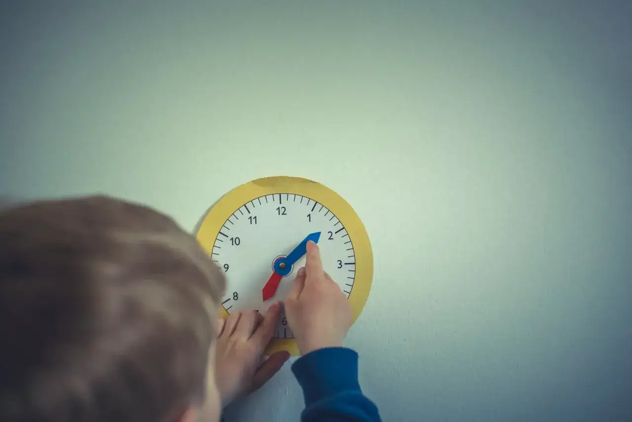 Dziecko uczy się odczytywać godzinę z zegara, co może pomóc w nauce jak przyspieszyć tempo pracy dziecka.