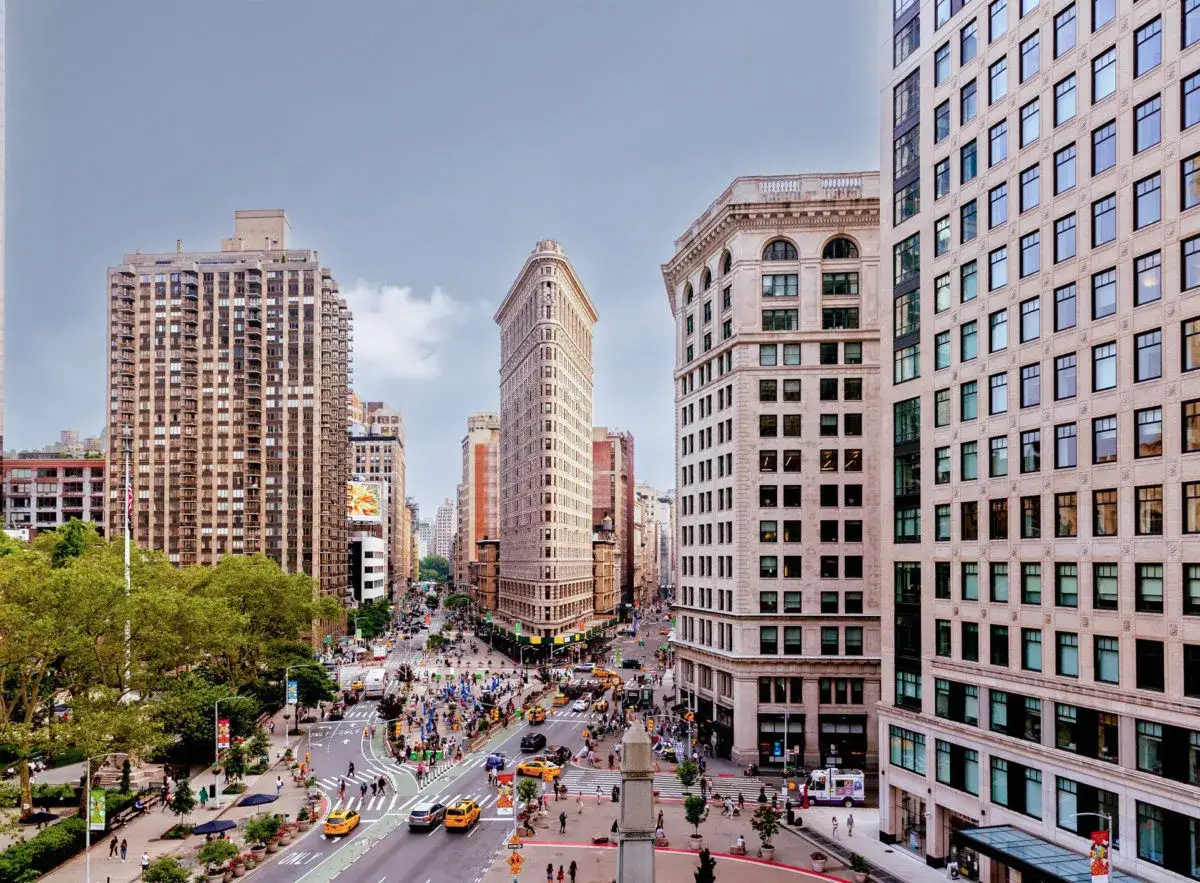 Vista aérea de la intersección de calles de Nueva York, con el icónico edificio Flatiron en el centro. Los planos de la ciudad se despliegan con tráfico y peatones.