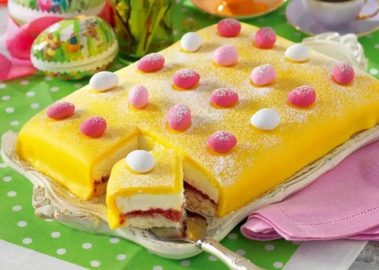 En gul p&aring;skt&aring;rta enkel, dekorerad med rosa och vita marsipan&auml;gg, pudrad med florsocker. En bit &auml;r uppskuren och visar lager av kr&auml;m och sylt.