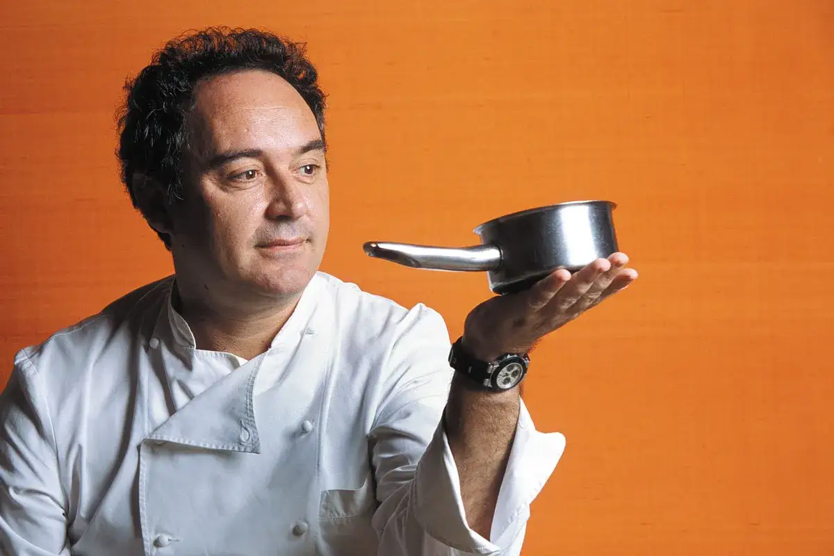 Chef catalán con estrellas Michelin, con una cazuela en la mano, sobre fondo naranja.