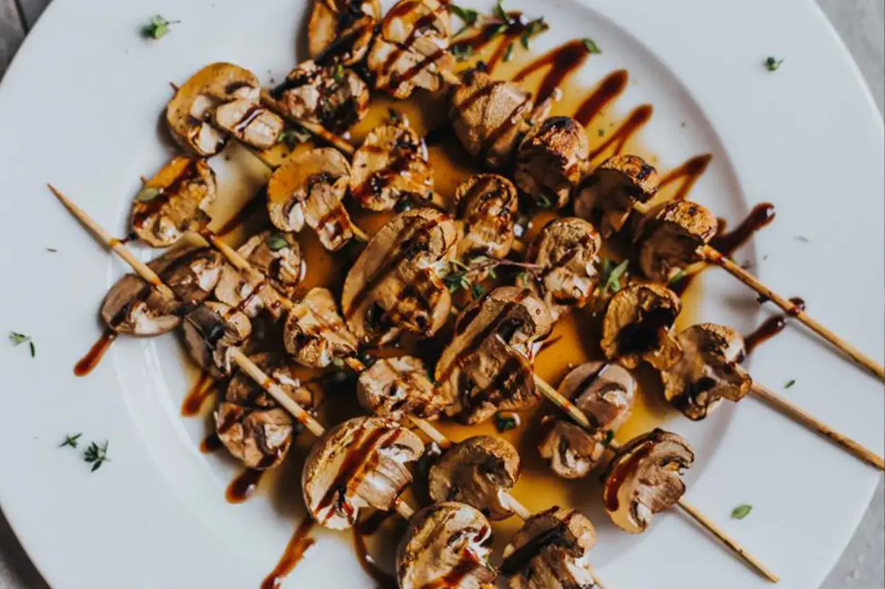 Gegrillte Champignons auf Spießen, beträufelt mit einer dunklen Soße und garniert mit Kräutern. Ein köstliches Gericht, das Lust auf mehr macht.