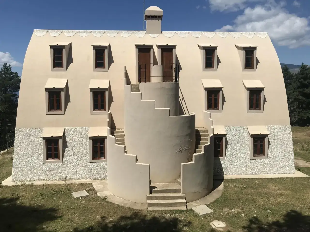 Edificio singular con escalinata exterior en espiral, ventanas simétricas y tejado curvo en la Serra de Catllaras.