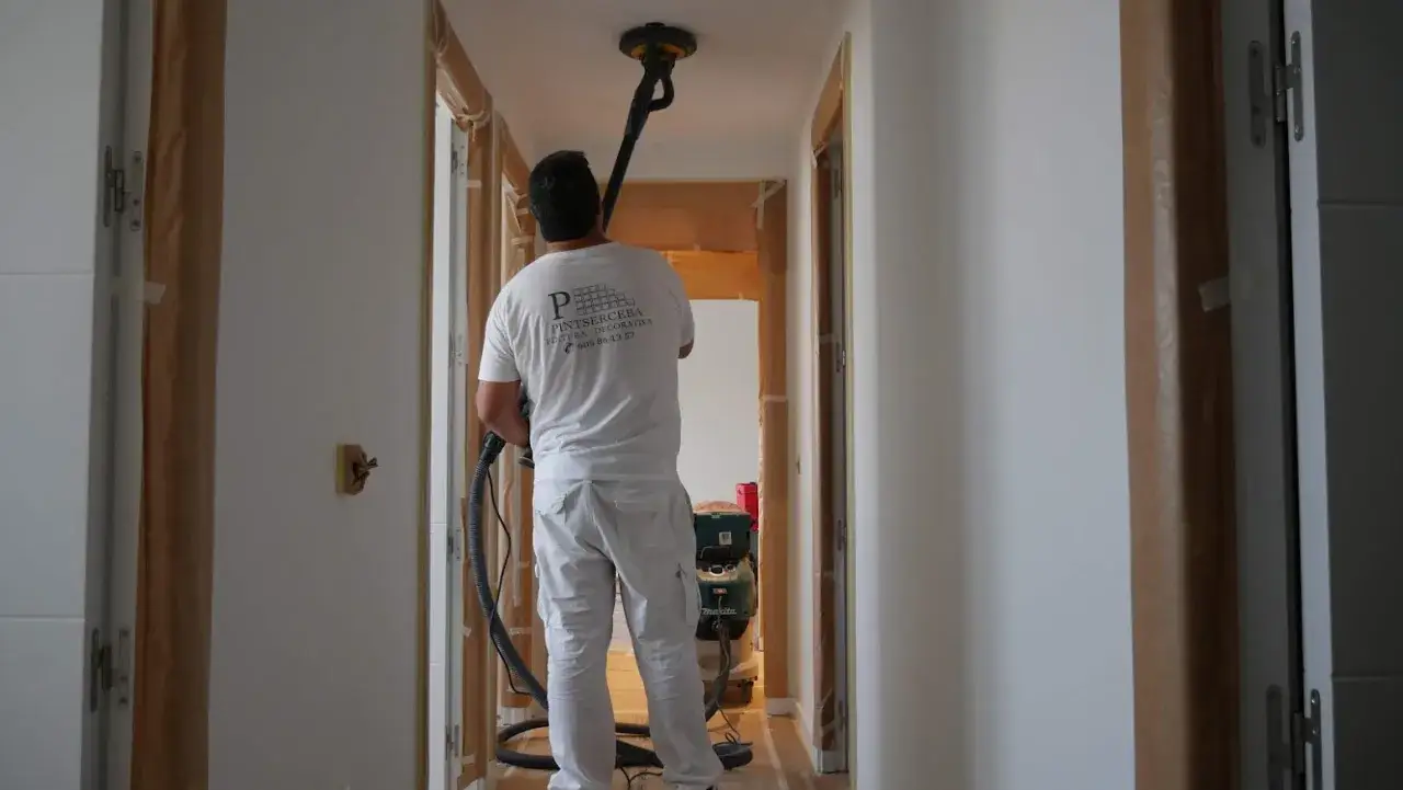 Pintor usando una lijadora de techo para alisar paredes en un pasillo.
