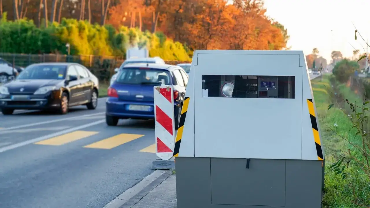 Blitzerwarner warnt vor m&ouml;glicher Strafe. Autos fahren auf der Stra&szlig;e an einem Blitzkasten vorbei.