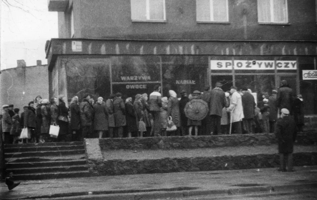 Kolejka do sklepu spożywczego w czasach komunizmu. Ludzie czekają na zakupy, widoczne napisy 
