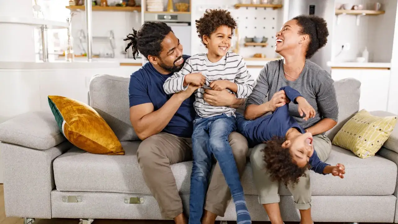 Eine lachende Familie auf dem Sofa. Dies zeigt, welche erziehungsstile es gibt: liebevoll und spielerisch.