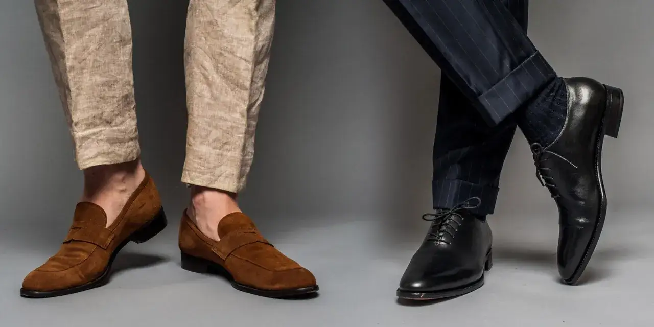 Deux paires de chaussures élégantes, un pantalon qui tombe sur la chaussure, l'une en daim marron, l'autre en cuir noir.