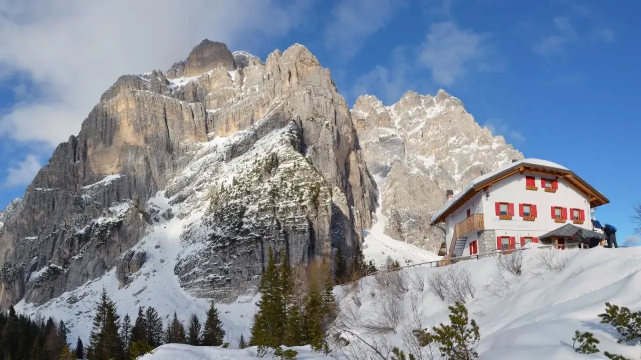 Rifugio Carestiato, un'oasi bianca sotto imponenti vette. Come arrivare? Segui la neve e le tracce degli escursionisti.
