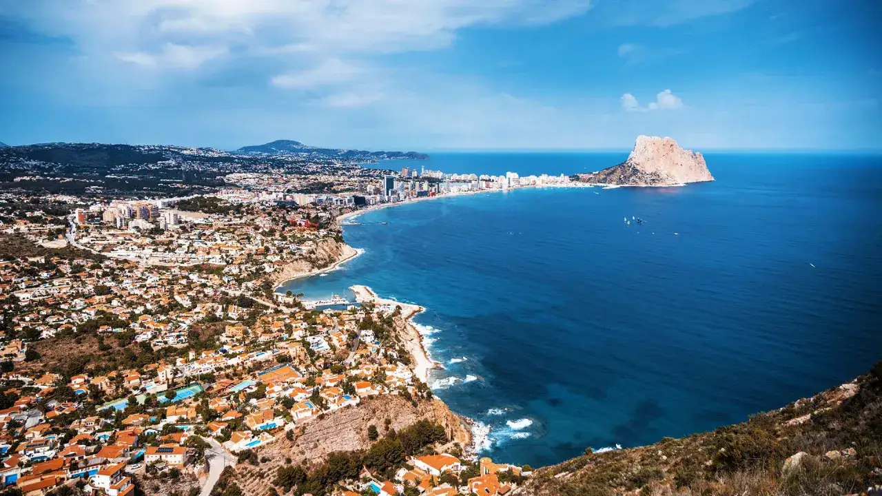 Blick auf die K&uuml;ste von Calpe, Spanien. Ein versteckter Juwel mit wei&szlig; get&uuml;nchten H&auml;usern, die sich an die H&auml;nge schmiegen, und dem ikonischen Felsen Pe&ntilde;&oacute;n de Ifach im Meer.