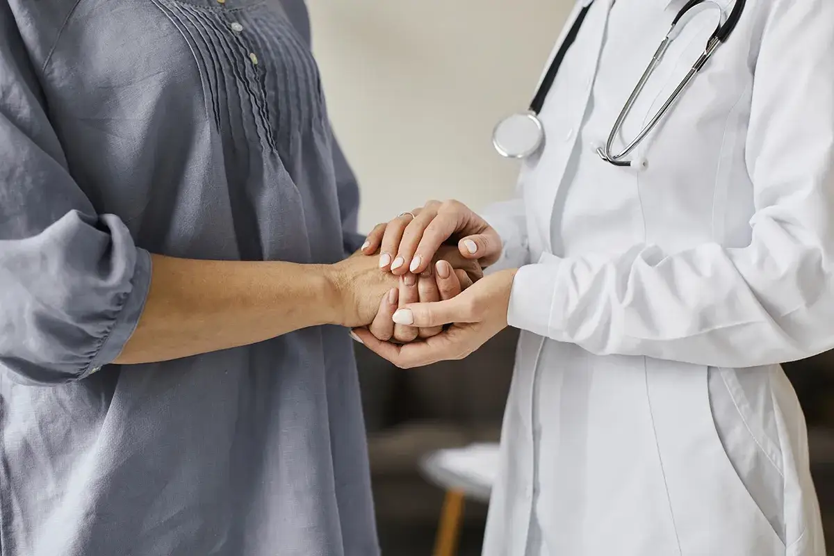 Lekarz w białym kitlu trzyma dłoń pacjentki, budując relację terapeutyczną.