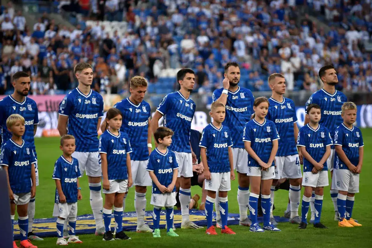 Piłkarze Lecha Poznań w niebieskich strojach stoją w rzędzie z dziećmi.