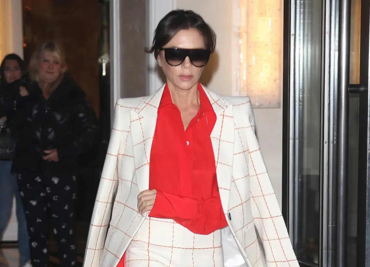 Victoria Beckham, con un traje de cuadros blanco y naranja y camisa roja, sale de un edificio.