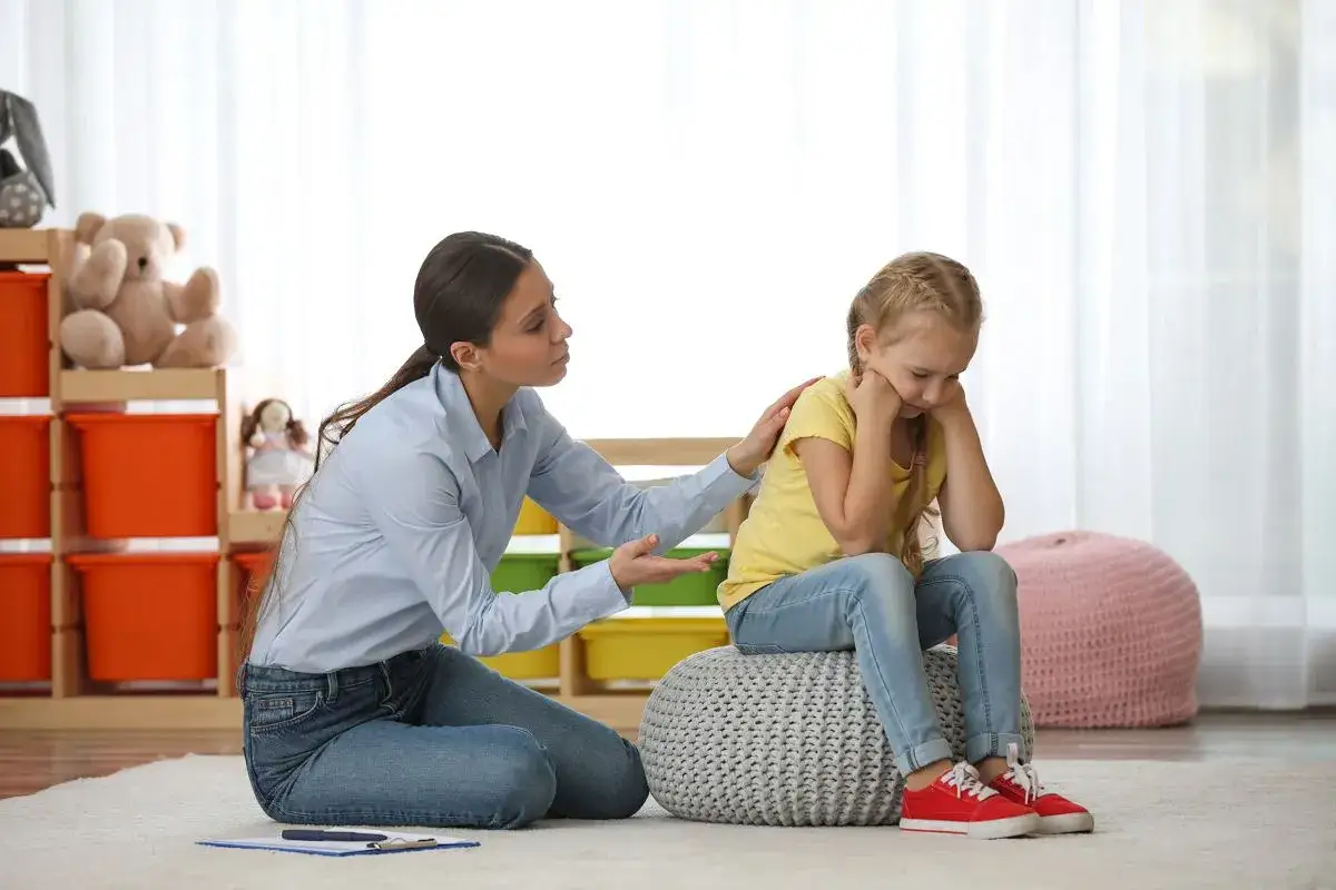 Terapeutka wspiera dziewczynkę, kt&oacute;ra może mieć objawy ADHD. Dziecko wygląda na smutne i przygnębione.