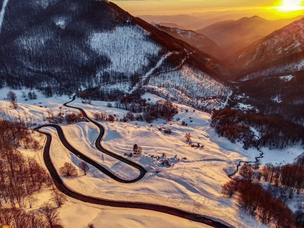 Strada tortuosa innevata nell'Appennino Tosco Emiliano, perfetta per un'avventura in moto al tramonto.