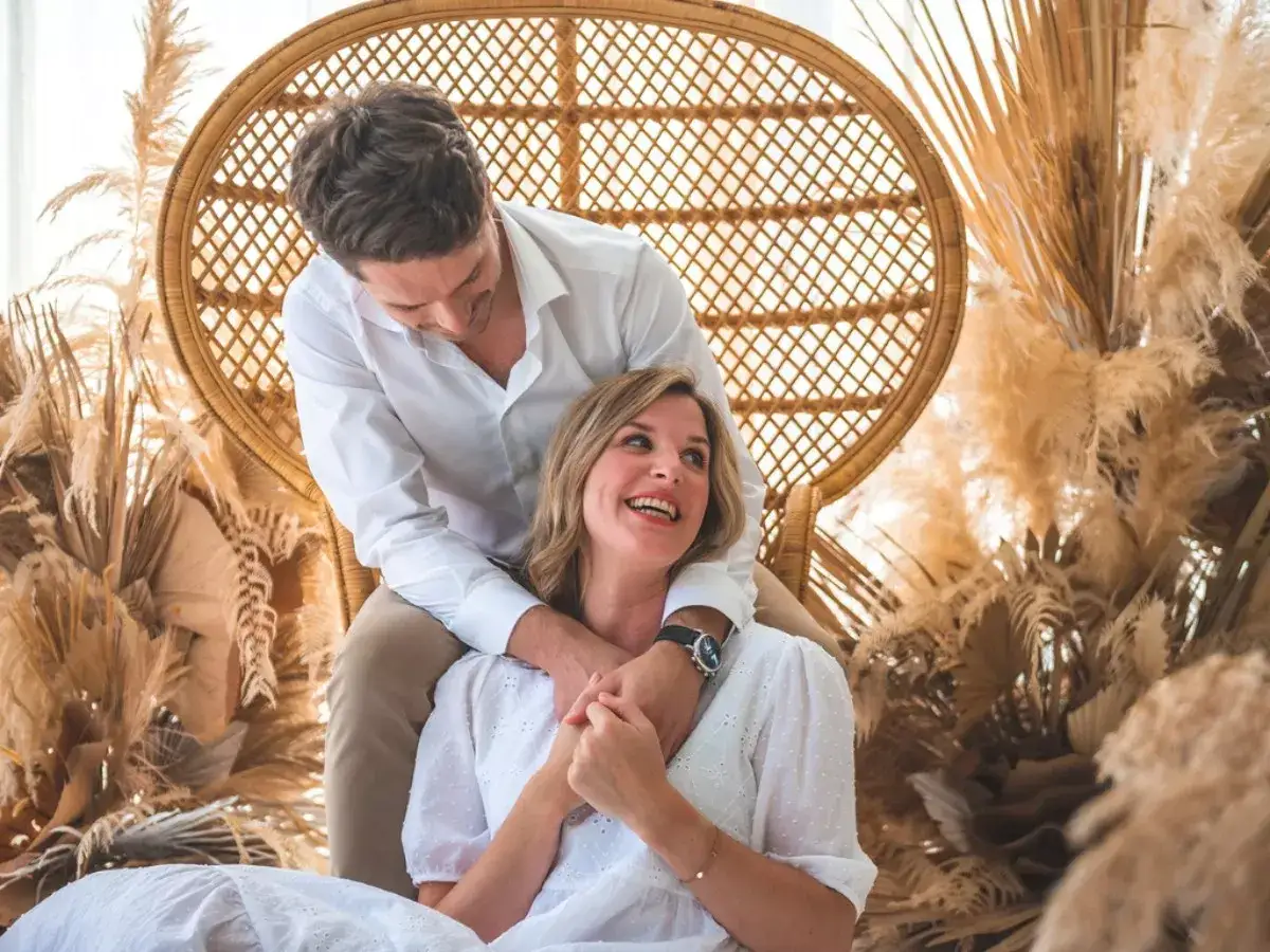 Pareja feliz celebrando 2 años de casados, abrazados en una silla de mimbre rodeados de pampas secas.