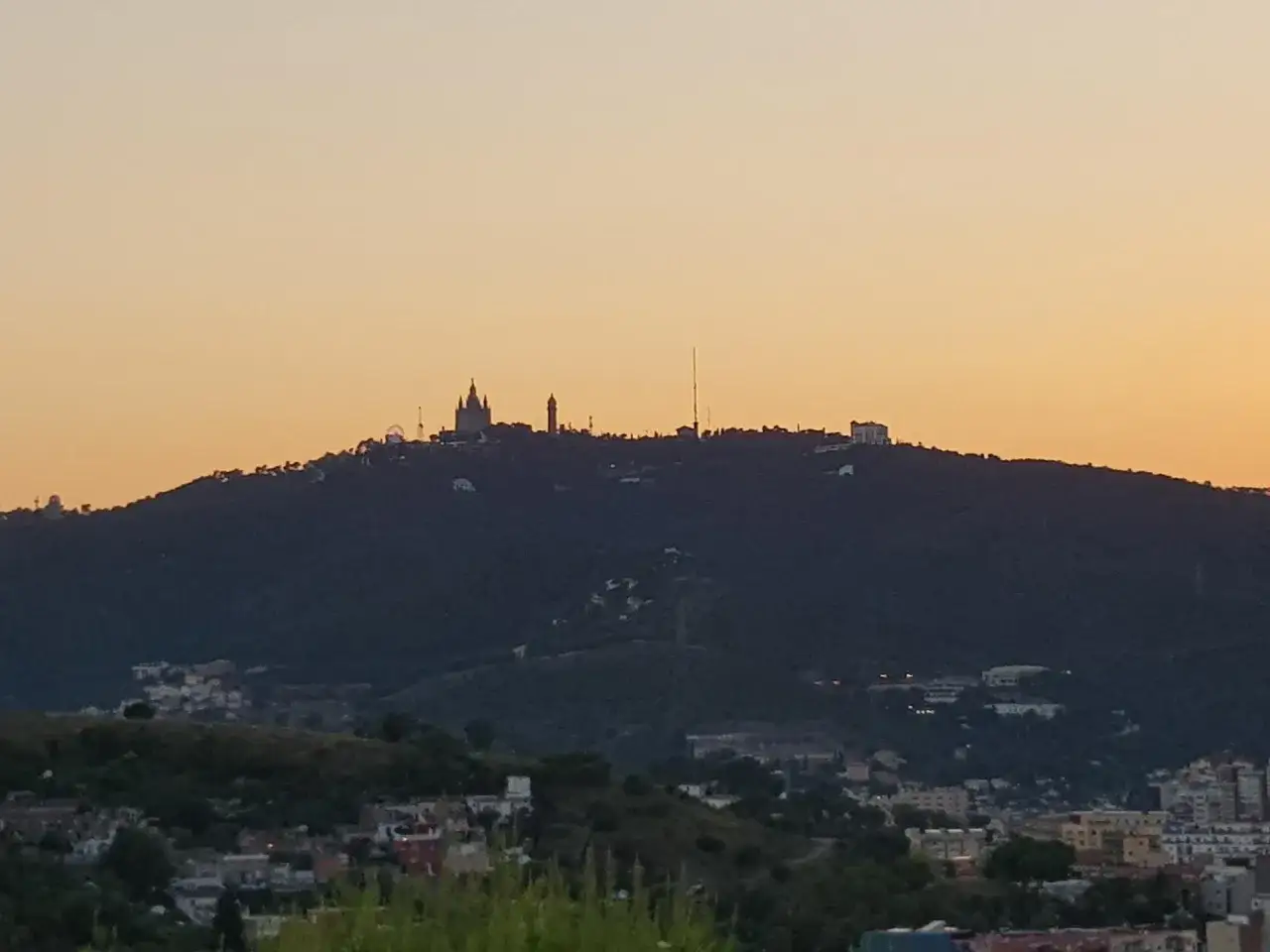 Silhouetten von Geb&auml;uden auf einem H&uuml;gel bei Sonnenuntergang, die die Barcelona Natur &uuml;berblicken.
