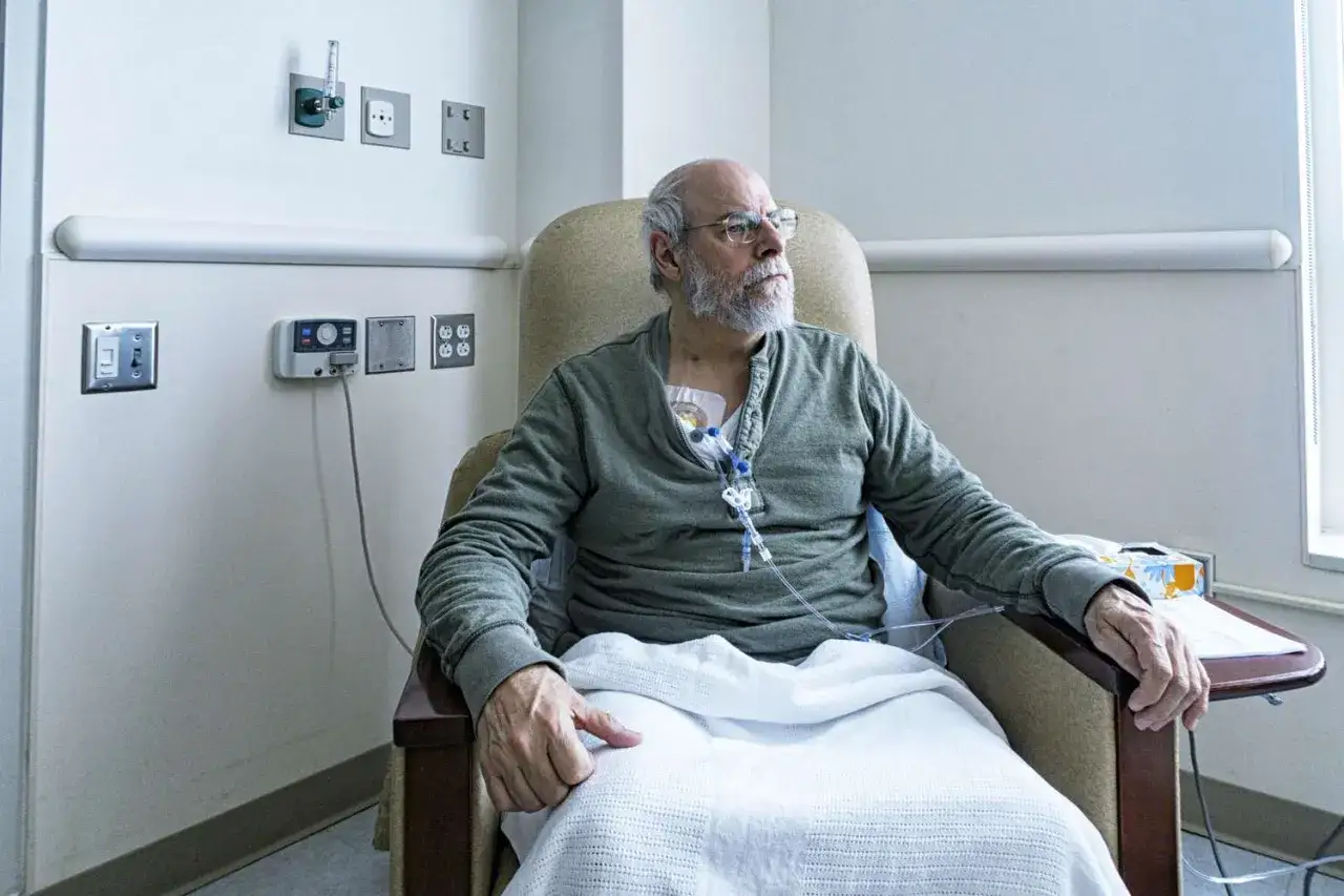 Ein Mann sitzt in einem Sessel, bedeckt mit einer Decke, und erh&auml;lt eine Infusion. Er unterzieht sich einer Chemoimmuntherapie.