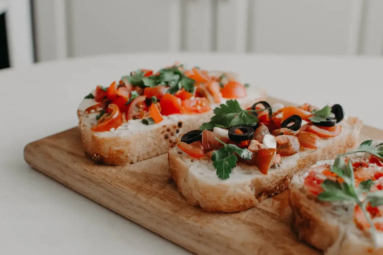 Tre l&auml;ckra bruschettor med tomat, basilika och oliver p&aring; en tr&auml;sk&auml;rbr&auml;da. Ett perfekt bruschetta recept f&ouml;r sommaren.