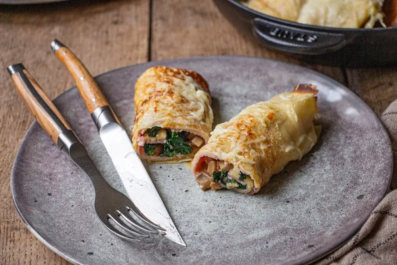 Deux cr&ecirc;pes garnies de jambon, &eacute;pinards et champignons, gratin&eacute;es au fromage et &agrave; la b&eacute;chamel au four. Servi avec une fourchette et un couteau.