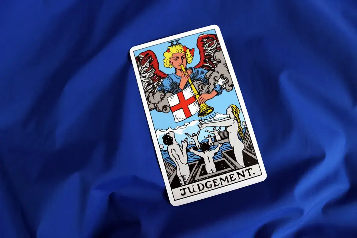 Karta Sąd Ostateczny Tarot. Anioł gra na trąbie, budząc ludzi do życia.