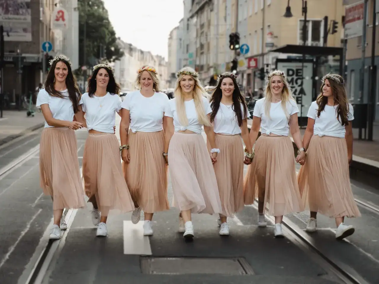 Sieben Frauen mit Blumenkränzen und passenden Röcken überqueren fröhlich eine Straße. Ein toller Geheimtipp für einen Junggesellenabschied!