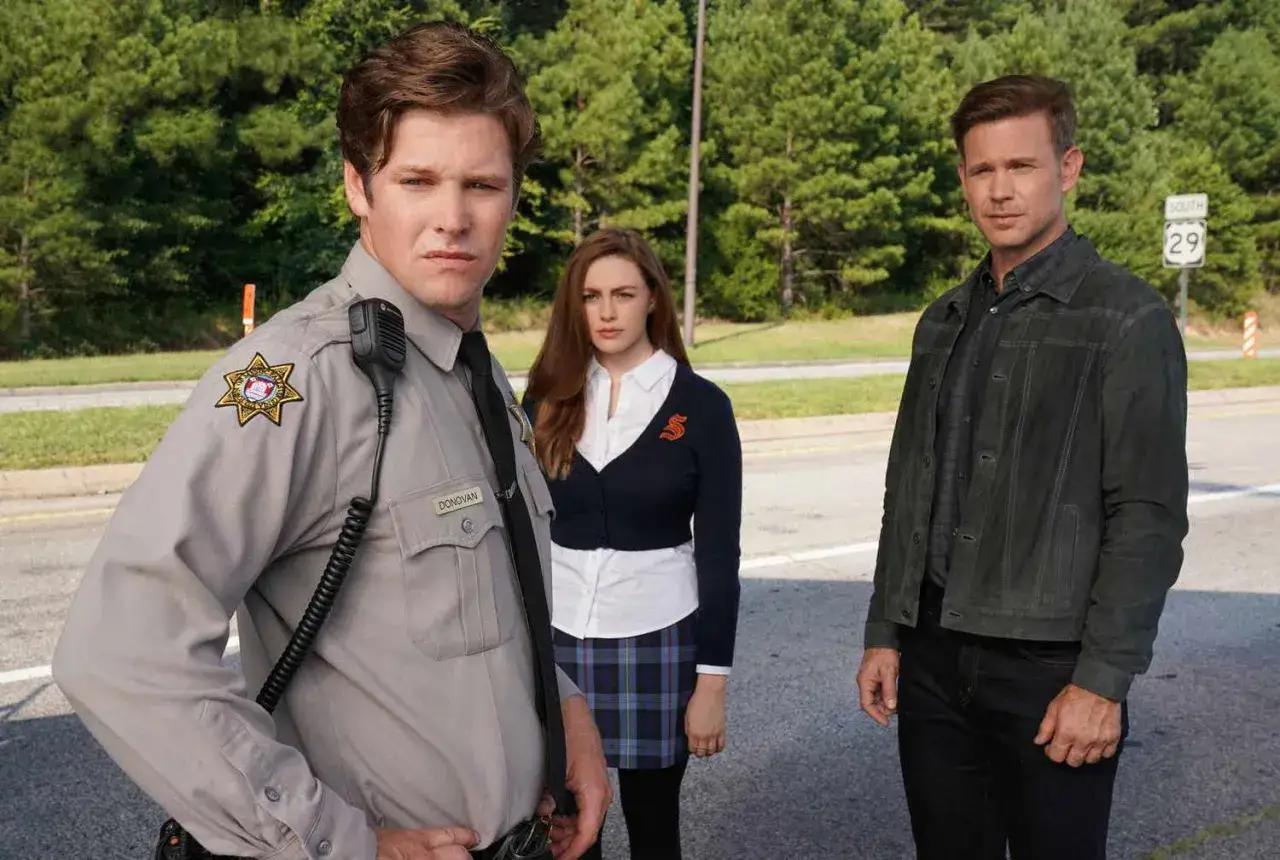 Trois personnages, dont un policier, une jeune femme en uniforme scolaire et un homme en veste, posent pour une sc&egrave;ne de Legacies saison 5.
