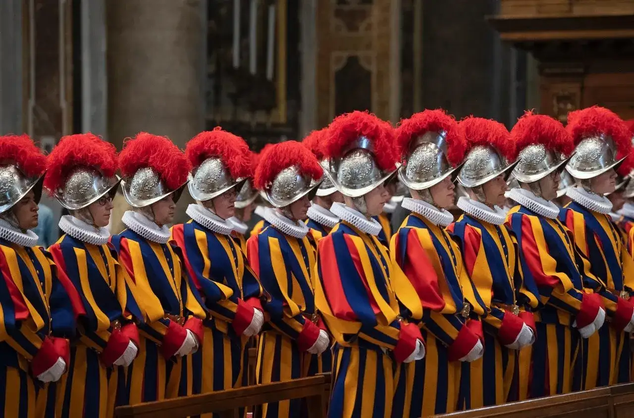 Guardia svizzera pontificia in divisa storica, con elmi piumati e abiti a righe blu e gialle, in posa solenne.