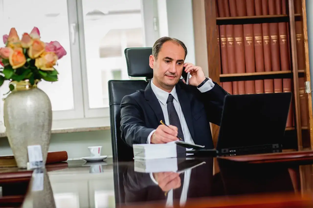 Radca prawny w garniturze rozmawia przez telefon, notując coś w zeszycie. Czy radca prawny może być obrońcą? Tak, jego wiedza prawnicza jest kluczowa.