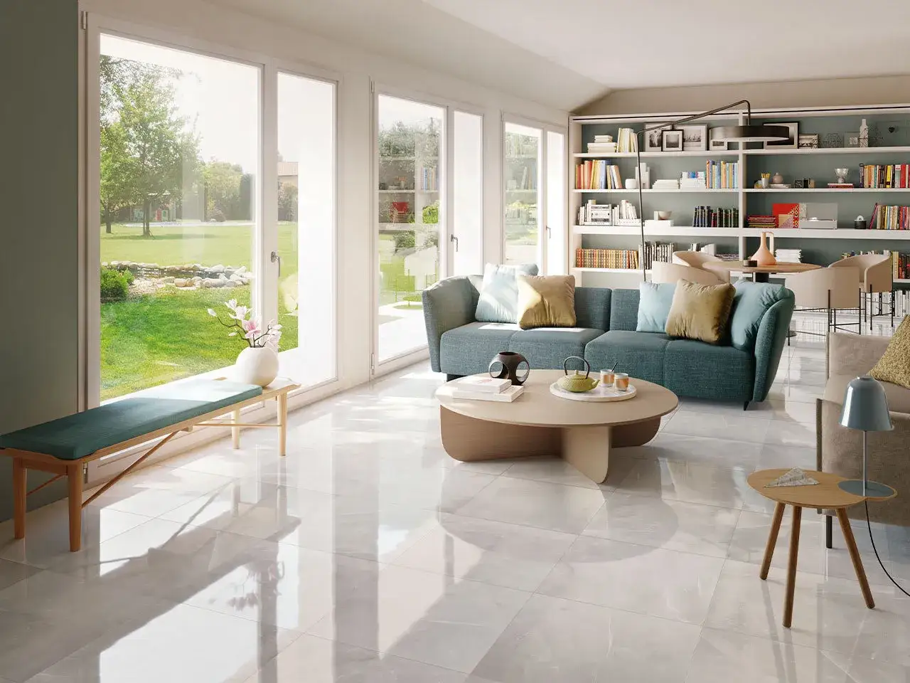 Soggiorno luminoso con divano blu, libreria piena e un ampio **pavimento lucido** che riflette la luce del sole e il verde del giardino.