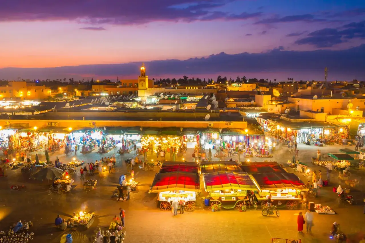 Der belebte marrakesch marktplatz erwacht bei D&auml;mmerung zum Leben. St&auml;nde mit bunten Waren, Essensverk&auml;ufer und Menschenmassen beleuchten die Nacht.