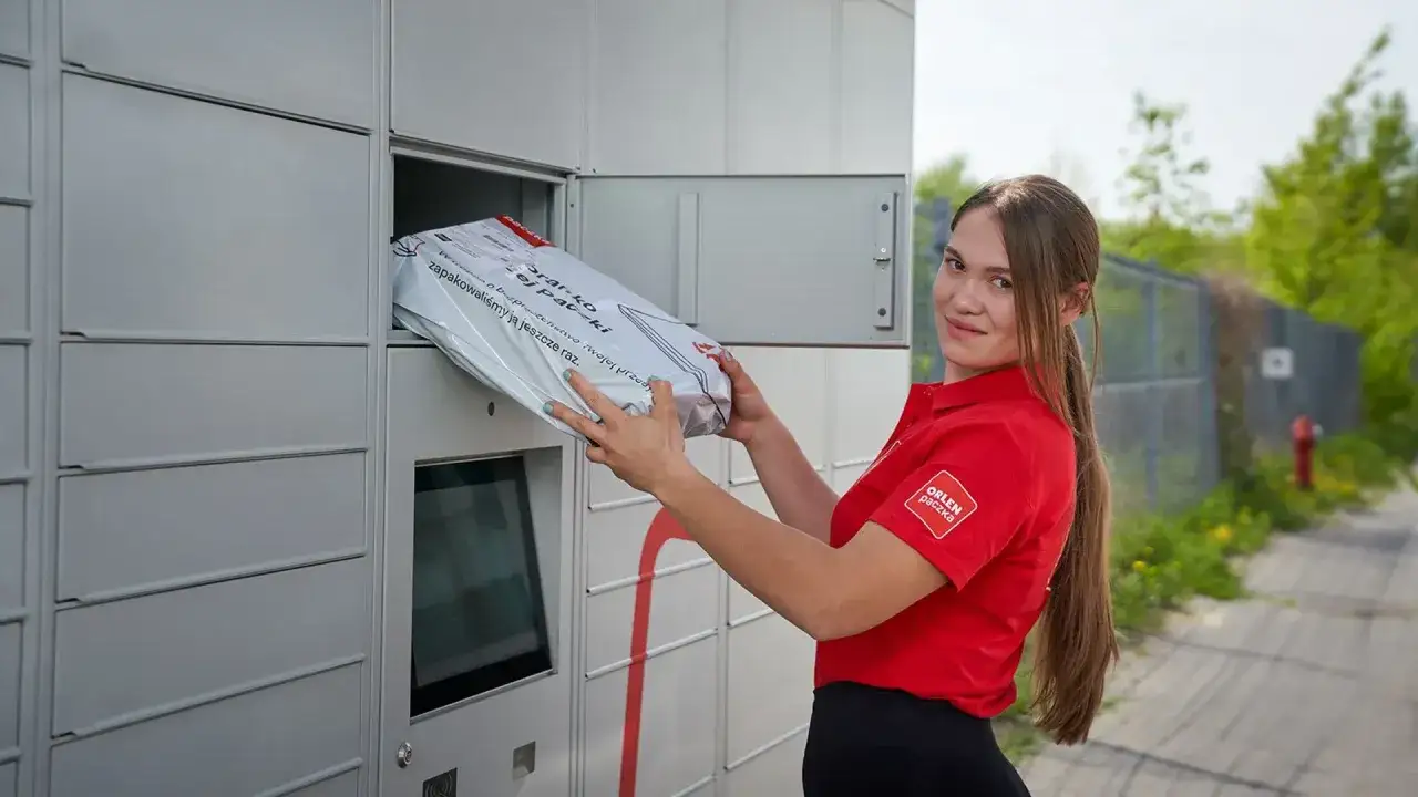 Uśmiechnięta kurierka Orlen Paczka wkłada paczkę do automatu. Zastanawiasz się, ile zarabia kurier?