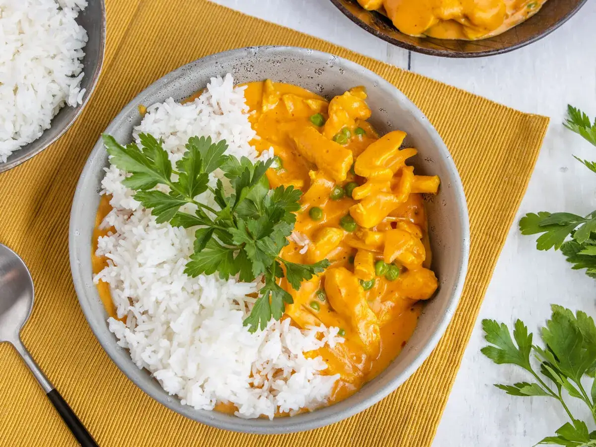 Sch&uuml;ssel mit Reis und cremigem Curry Geschnetzeltes, garniert mit Petersilie.