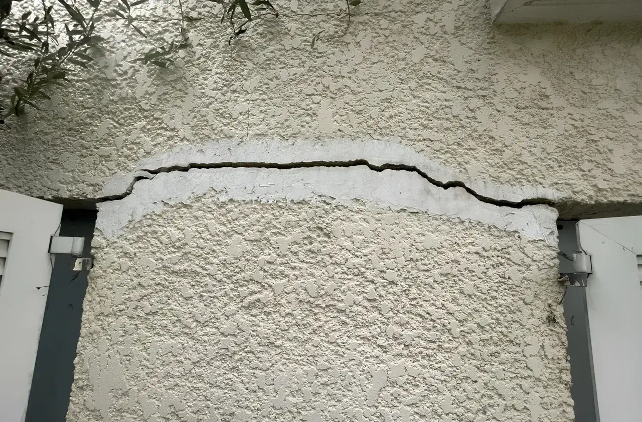 Grosse fissure sur un mur extérieur, signe qu'il faut réhabiliter une maison. Des branches d'arbre surplombent.