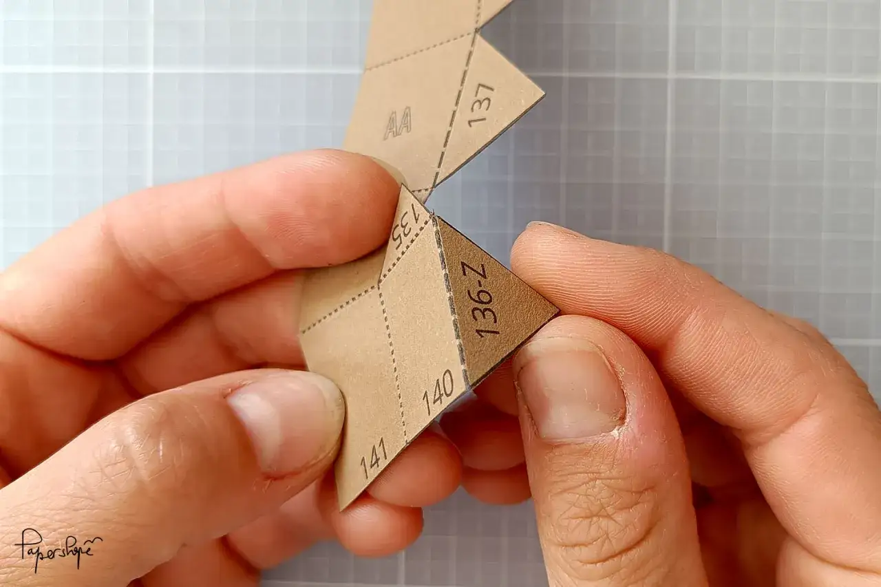 Hände falten ein Papier mit Zahlen und Buchstaben. Die Anleitung zum berge aus papier falten wird präzise befolgt.