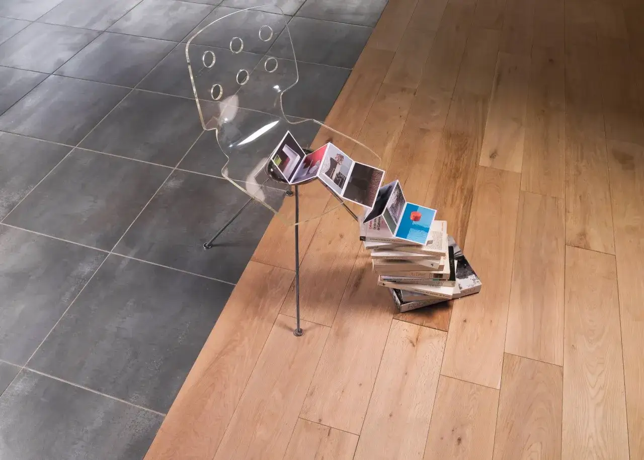 Jonction carrelage parquet sans barre de seuil. Chaise transparente, livres ouverts et empil&eacute;s sur un parquet clair.