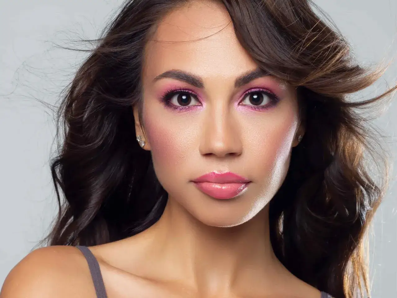 Un maquillage rose et doré sublime le regard et les lèvres d'une femme aux cheveux bruns ondulés.