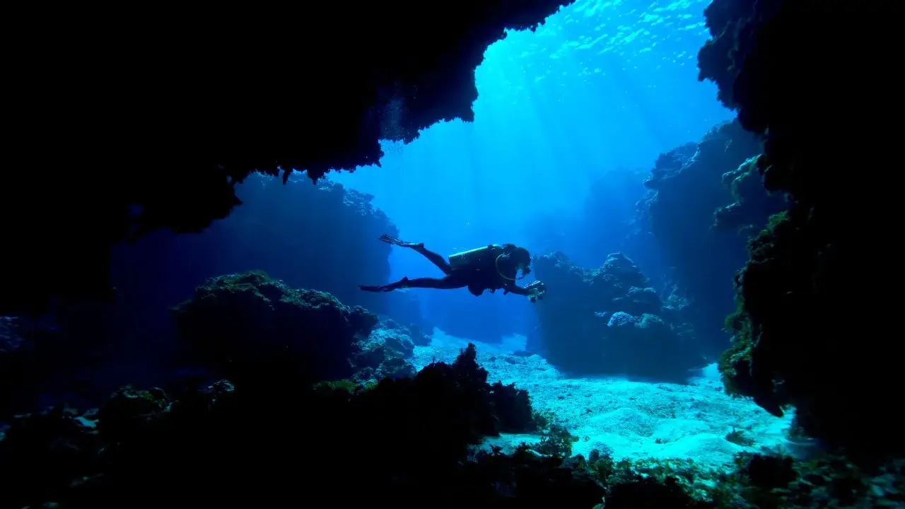 Nurkowie eksplorują podwodną jaskinię, odkrywając jedne z najlepszych miejsc do nurkowania. Promienie słońca przebijają się przez wodę, oświetlając skaliste dno.