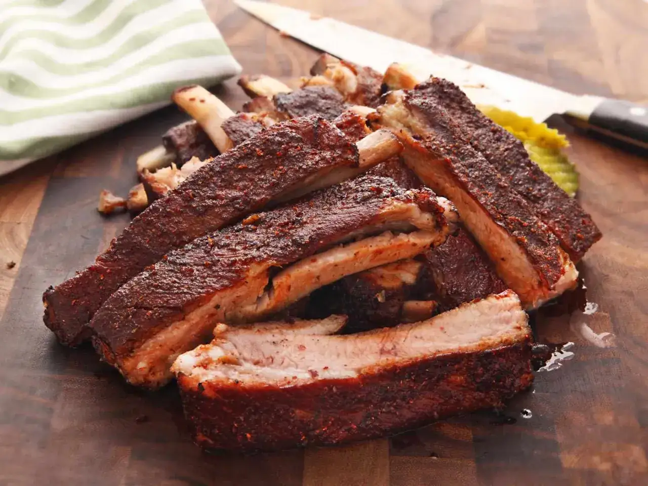 Un tas de ribs de porc grillés, assaisonnés et juteux, prêts à être dégustés. Un couteau et une serviette sont visibles en arrière-plan.